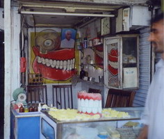 Another dentist, what you see is what you get, this is reception, examination room & store. The dentist usually sits in one of the kitchen chairs until he vacates to let the patient sit. The indistinct yellow things in the foreground are molds of people's mouths. 